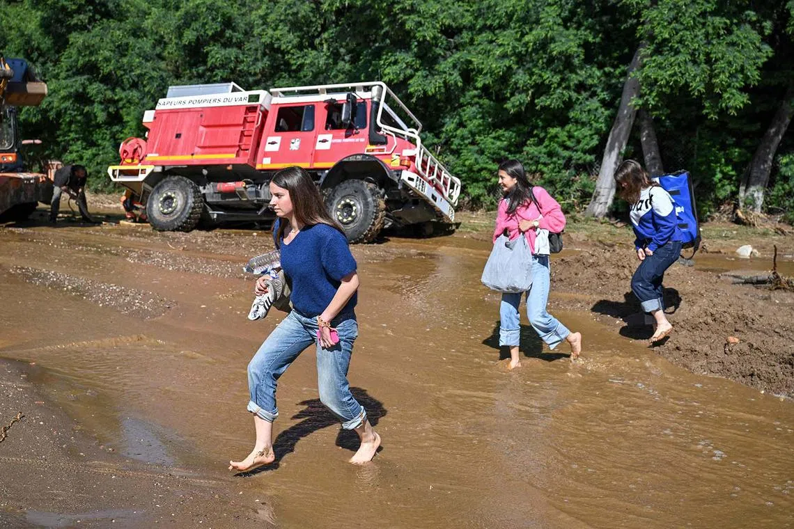 People walking through the water to cross a mud-covered road as a firefighting vehicle gets stuck in the mud following a flood caused by heavy rain in Cavaliere village, southeastern France, on May 20, 2025. 