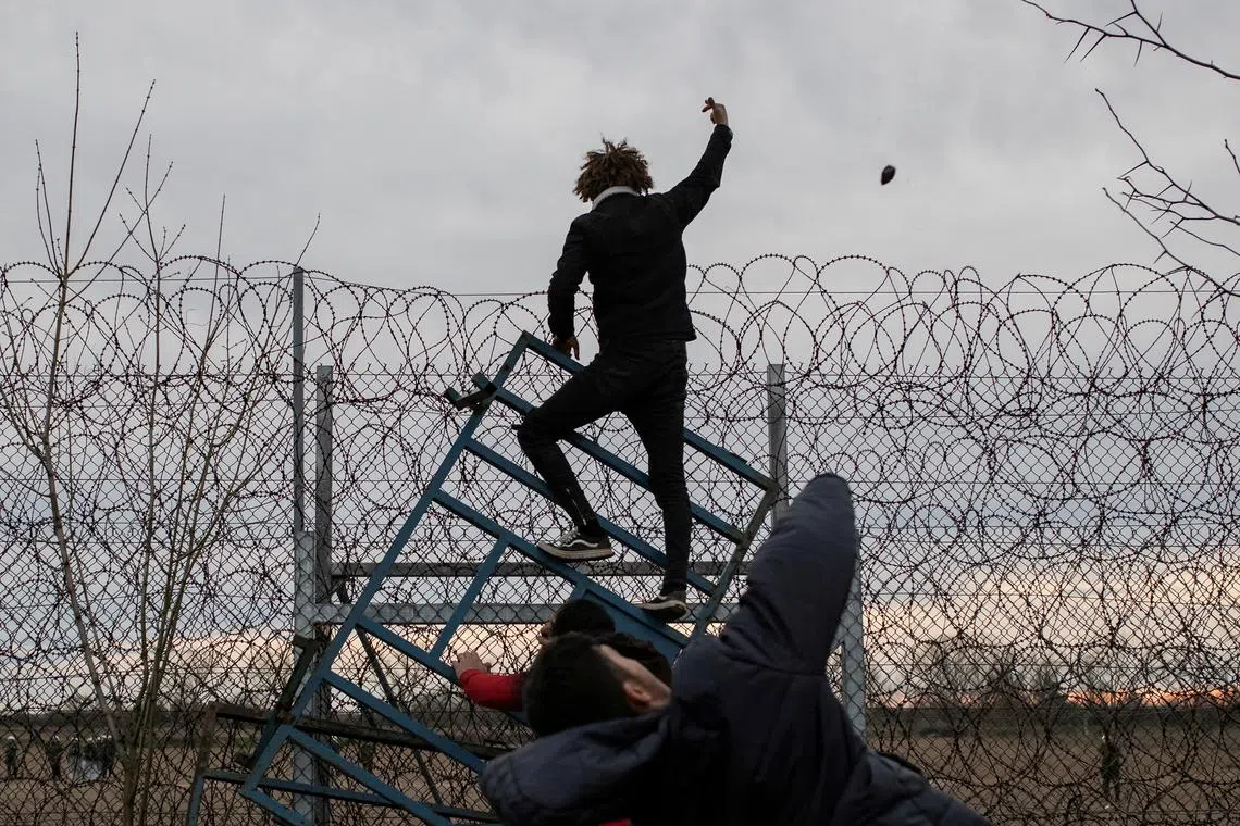 FILE PHOTO: A migrant throws a stone, while others climb a fence at the border, as they clash with Greek riot police at Turkey's Pazarkule border crossing with Greece's Kastanies, near Edirne, Turkey, March 6, 2020. REUTERS/Marko Djurica/File Photo