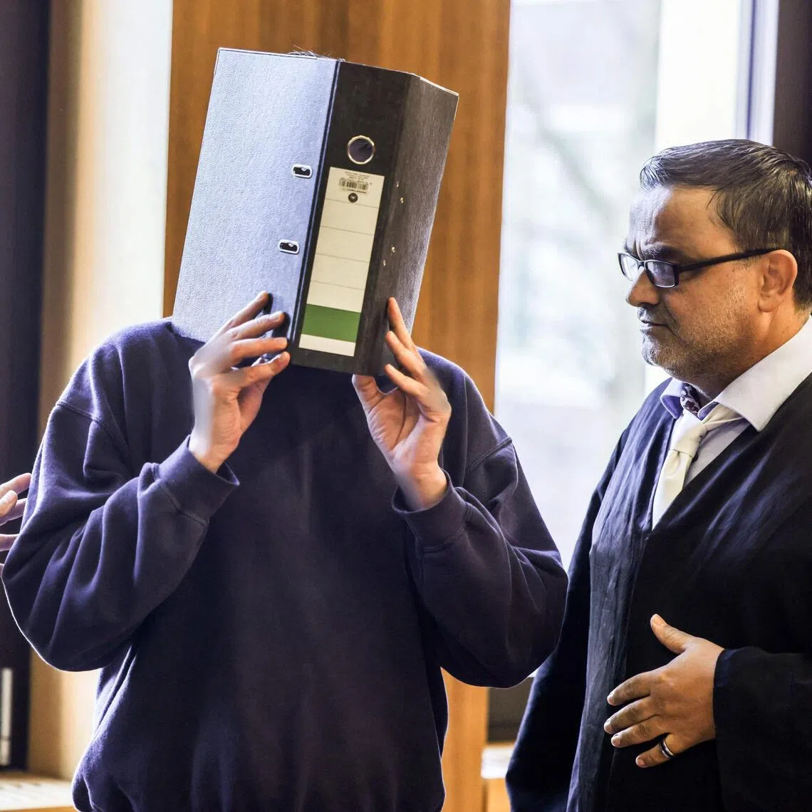 The accused former nurse hiding his face behind a folder next to his lawyer, Mr Volker Breyer (right), as he arrives in court on Nov 5.