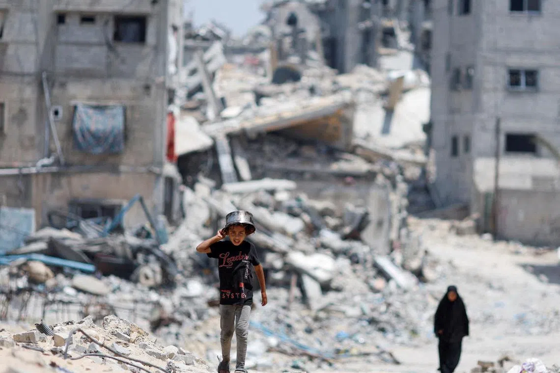 FILE PHOTO: Palestinians walk by houses which were destroyed in an Israeli strike, amid the ongoing conflict between Israel and Hamas, in Khan Younis, in the southern Gaza Strip, May 22, 2024. REUTERS/Mohammed Salem/File Photo