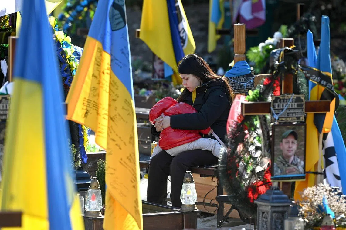 A woman and child sits among graves at the Lychakiv military cemetery in Lviv, Ukraine.