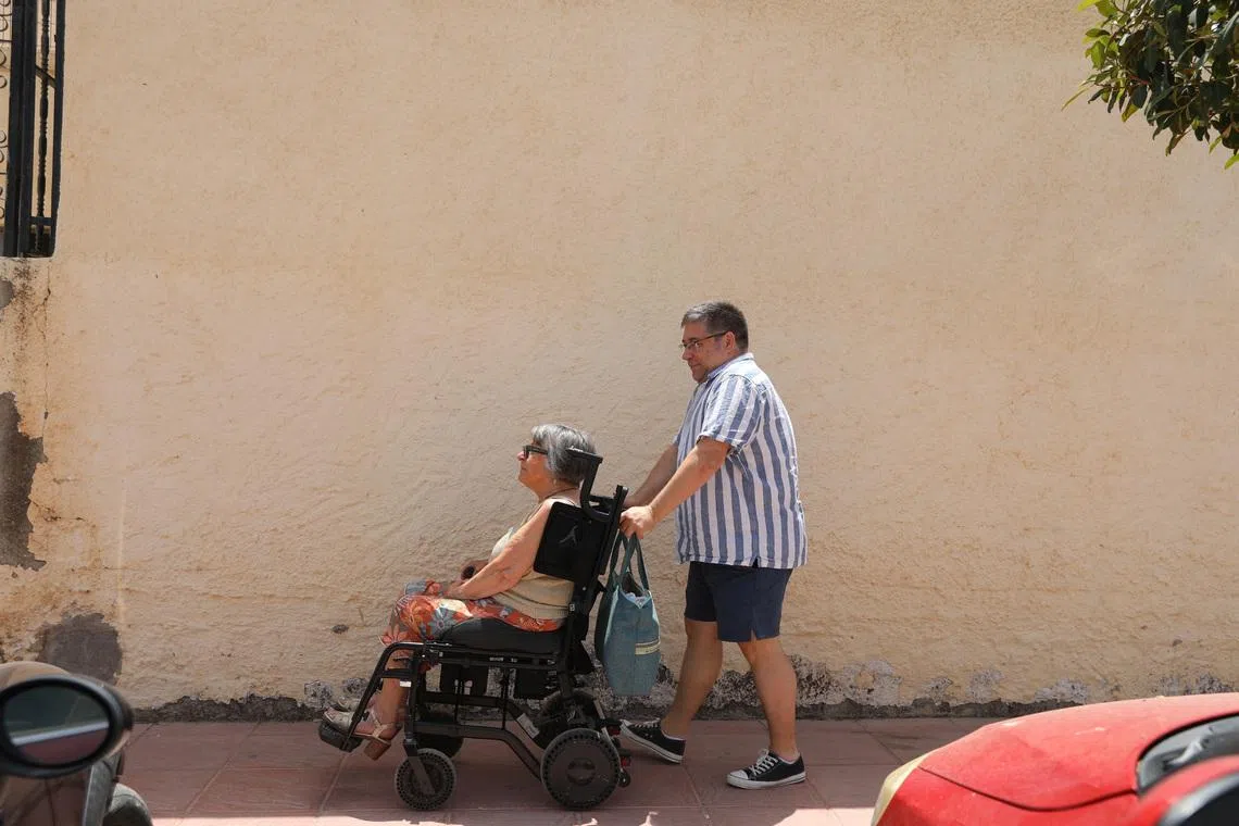 Daniel Northover, 53, who moved from Britain to Spain to care for his mother after her husband's death, takes his mother Carole Bentley, 80, for a walk in her wheelchair along a street in the village of Turre, Almeria, Spain, June 18, 2026. REUTERS/ Loyola Perez de Villegas Muniz