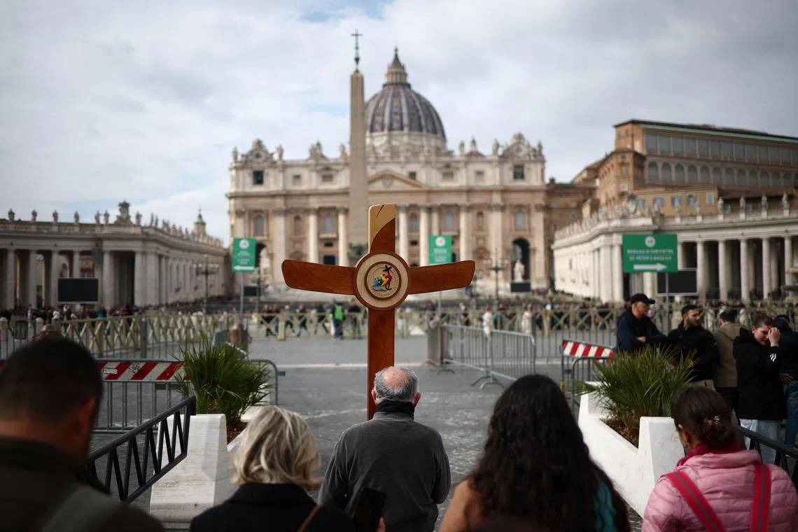 A pilgrims carries a cross as Pope Francis is admitted to continue treatment for a respiratory tract infection, at St. Peter's Square, in Vatican, February 18, 2025. REUTERS/Guglielmo Mangiapane