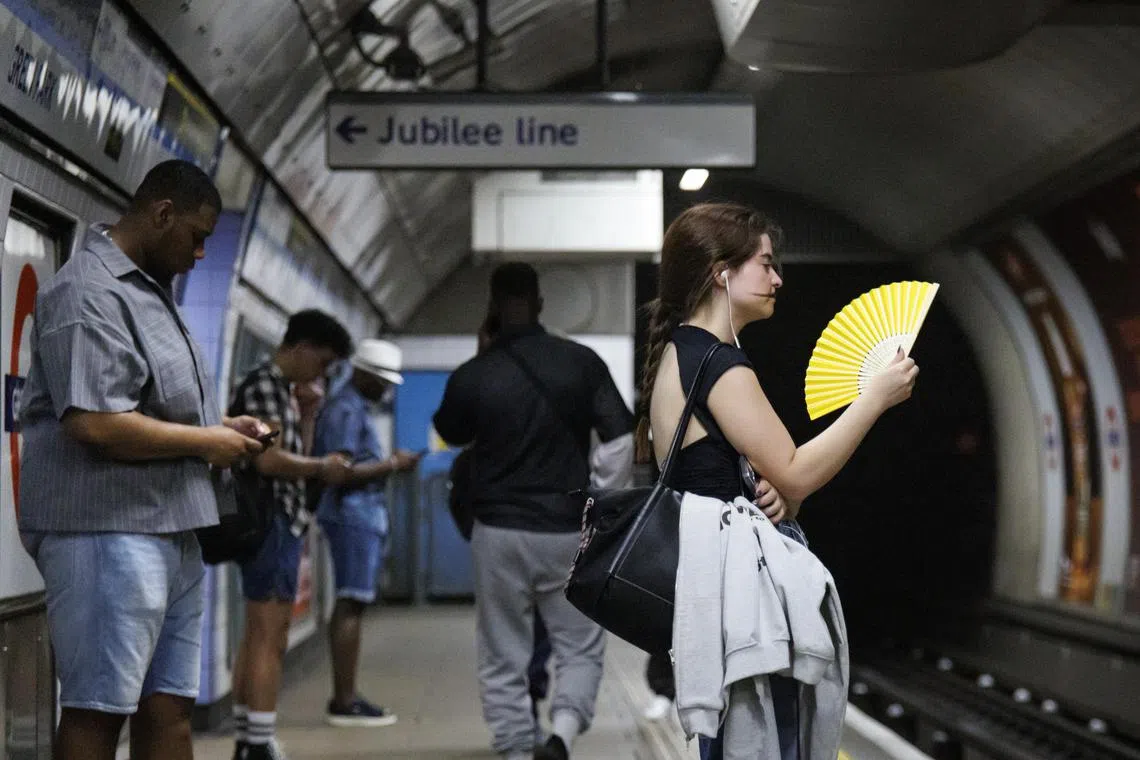 A person uses a fan to cool down as they wait for a Jubilee Line tube train on the London Underground in London.