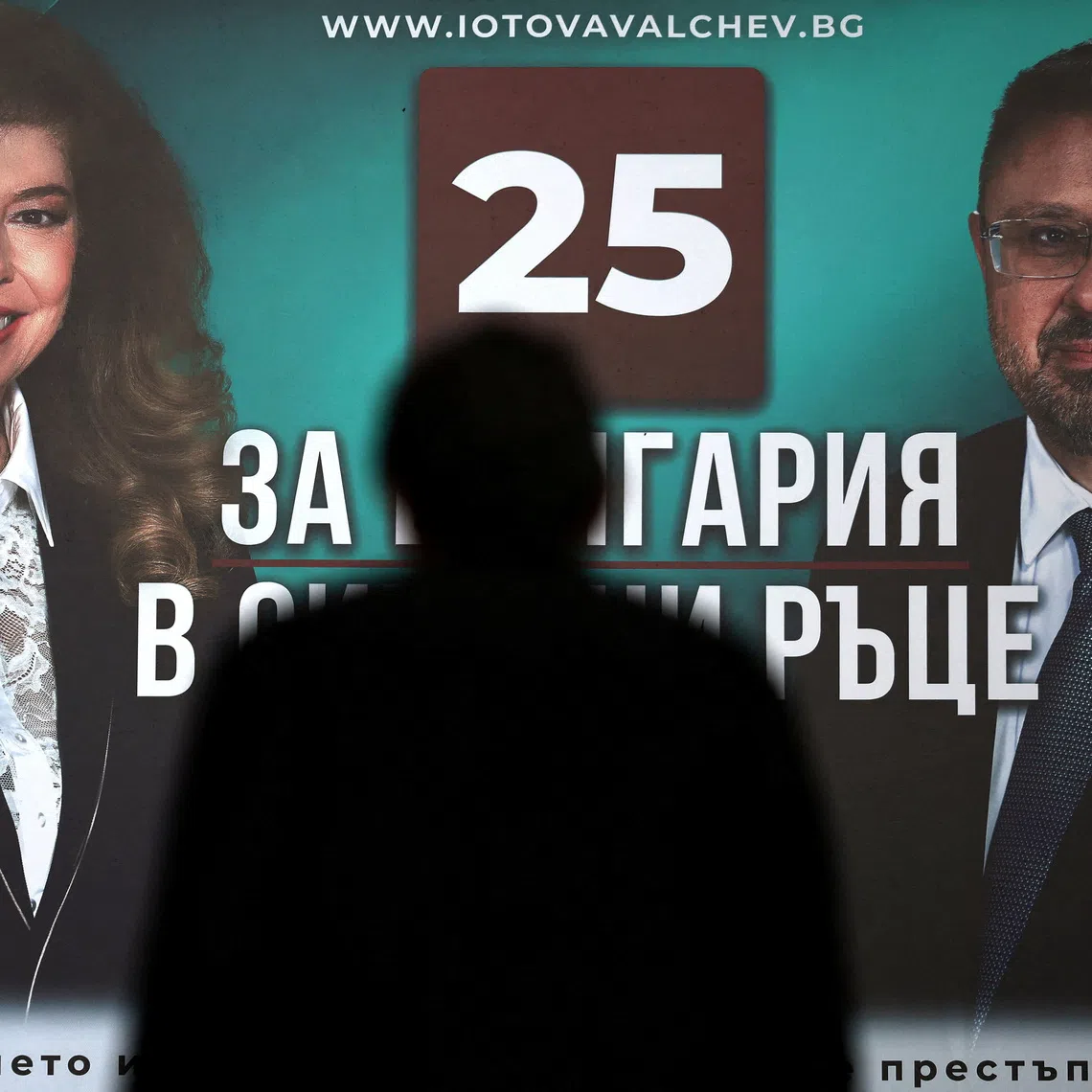 A person is silhouetted against an election billboard featuring Bulgarian presidential candidate and incumbent President Iliana Iotova and vice presidential candidate Kiril Valchev ahead of the country's presidential election on October 25, in Sofia, Bulgaria, October 22, 2026. REUTERS/Spasiyana Sergieva