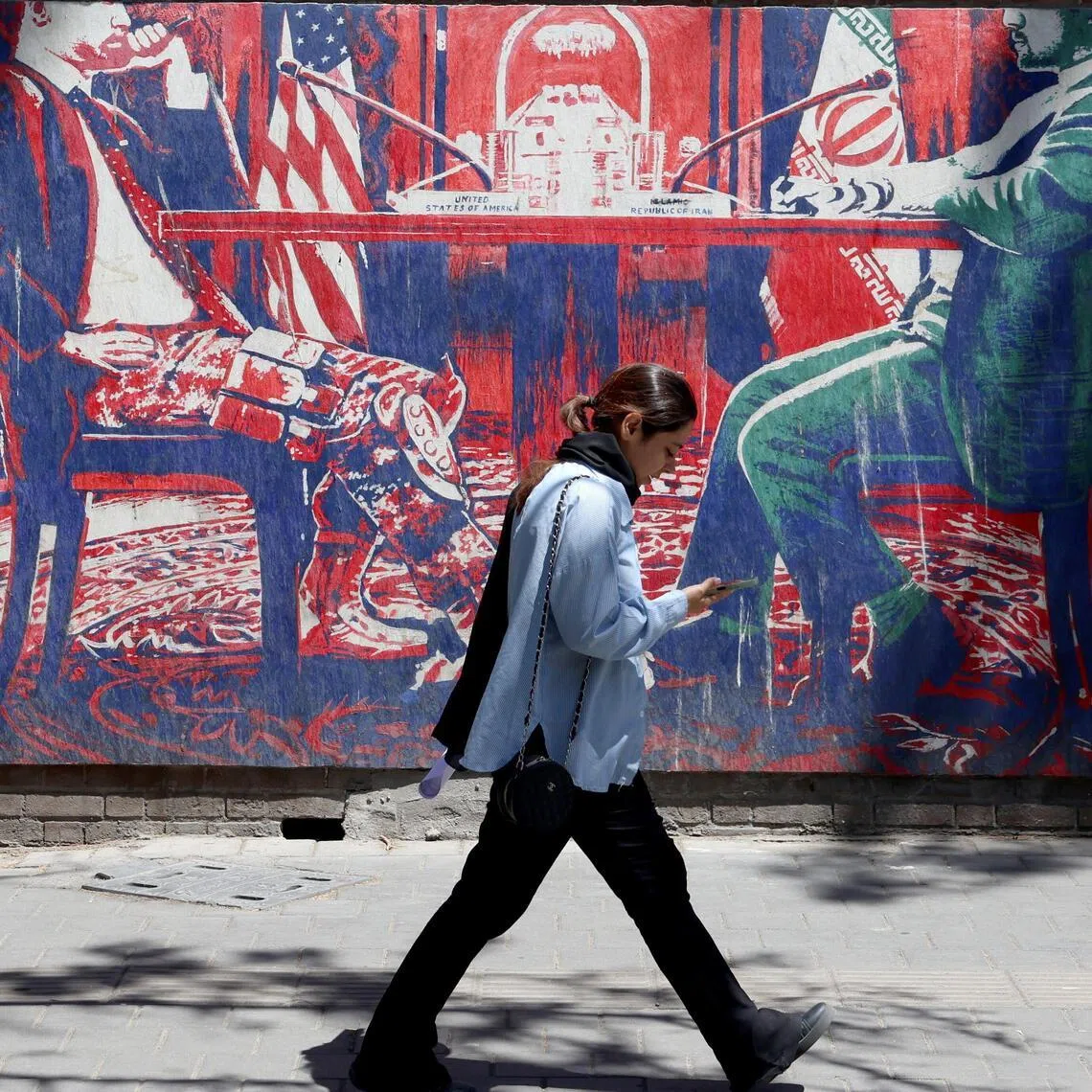 A pedestrian walks next to an anti-US mural depicting Iran and US negotiations, near the former US embassy in Tehran.
