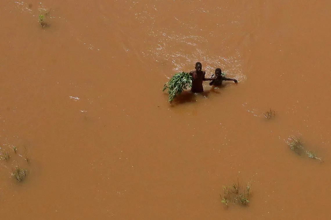 FILE PHOTO: FILE PHOTO: People hold on to plants as they wade through flood waters after they were displaced following heavy rains in Garsen, Tana Delta within Tana River county, Kenya November 23, 2023. REUTERS/Thomas Mukoya/File Photo