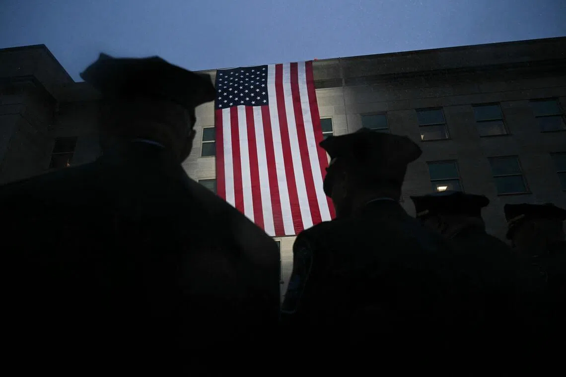 Military personnel and first responders watch as an American flag hangs from the side of the Pentagon.
