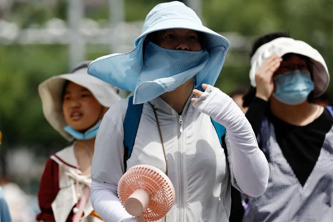 FILE PHOTO: People wearing sun protection gear amid a heatwave walk on a street in Beijing, China July 1, 2023. REUTERS/Tingshu Wang