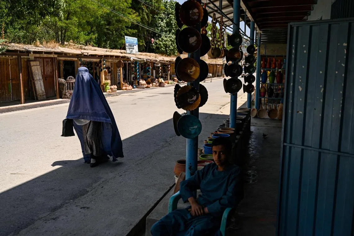 (FILES) An Afghan burqa clad women walks past shops selling clay bowls at a market in Istalif district in the northwestern Kabul province on July 3, 2023. Afghanistan has a centuries-old tradition of pottery across the country, but Istalif's reputation for craftsmanship and quality stands out. (Photo by Wakil Kohsar / AFP)