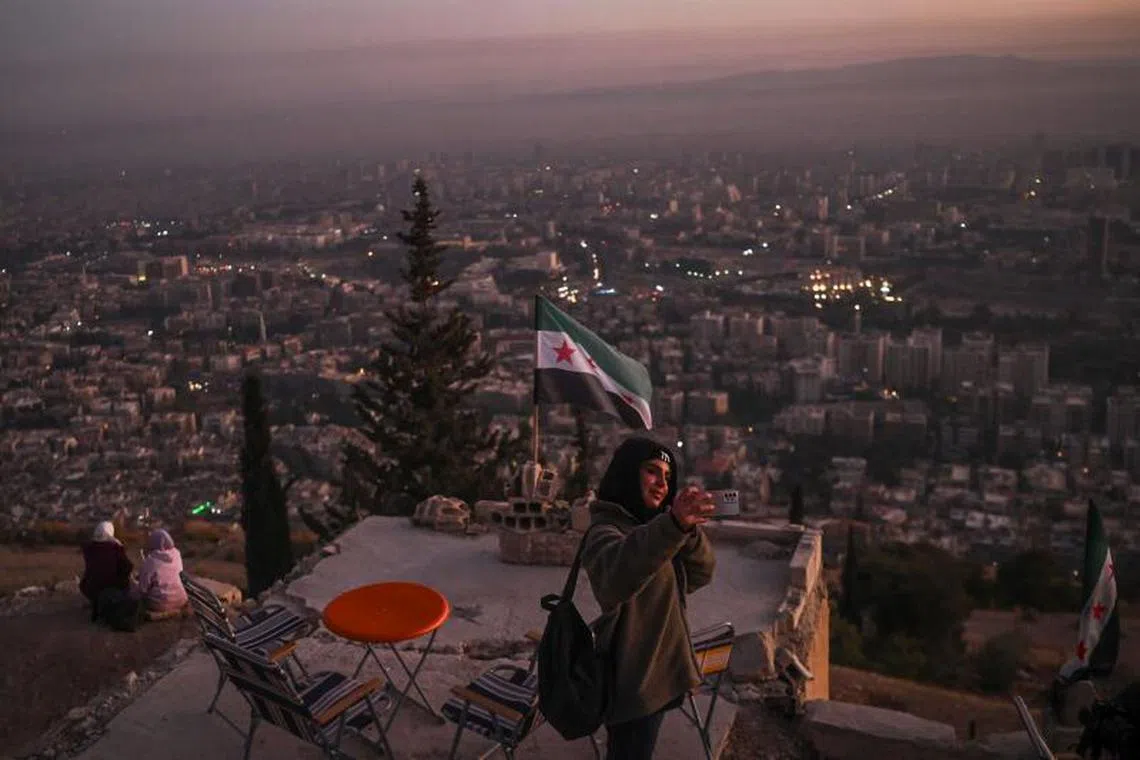 A woman takes a selfie as she stands on a hilltop overlooking the capital Damascus on December 18, 2024. Islamist-led rebels took Damascus in a lightning offensive on December 8, ousting president Bashar al-Assad and ending five decades of Baath rule in Syria. (Photo by Aris MESSINIS / AFP)