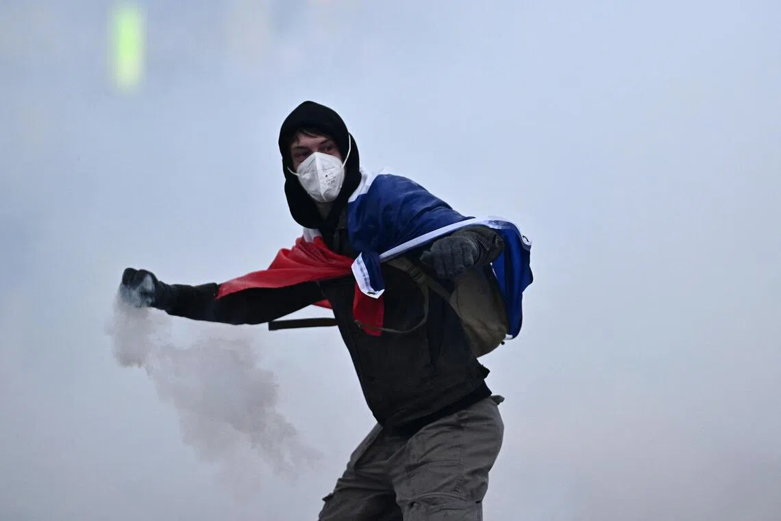 A masked protester wearing a French flag throws a tear gas canister in Paris on Oct 24.