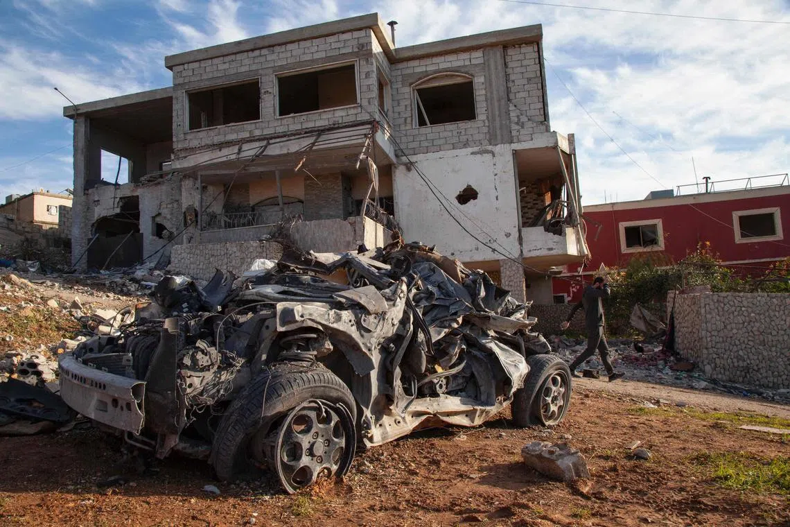 A man walks past a house and car damaged amid reported Israeli bombardment, in the southern Lebanese village of Kfar Kila.