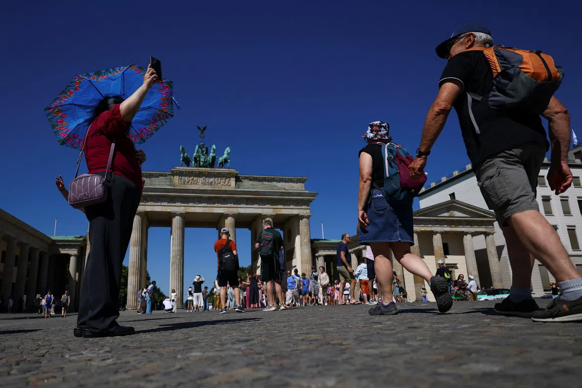 People shelter from the sun with umbrellas and hats as they visit the Brandenburg Gate on a hot summer day, as a heatwave hits Berlin, Germany, July 2, 2025. REUTERS/Lisi Niesner