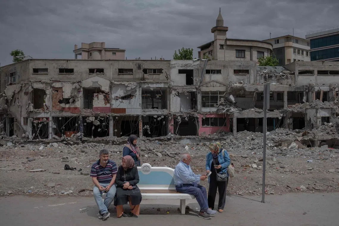 People wait at a bus stop in front of a destroyed building during the presidential runoff vote in the quake-hit city of Kahramanmaras, Turkey, on May 28, 2023.