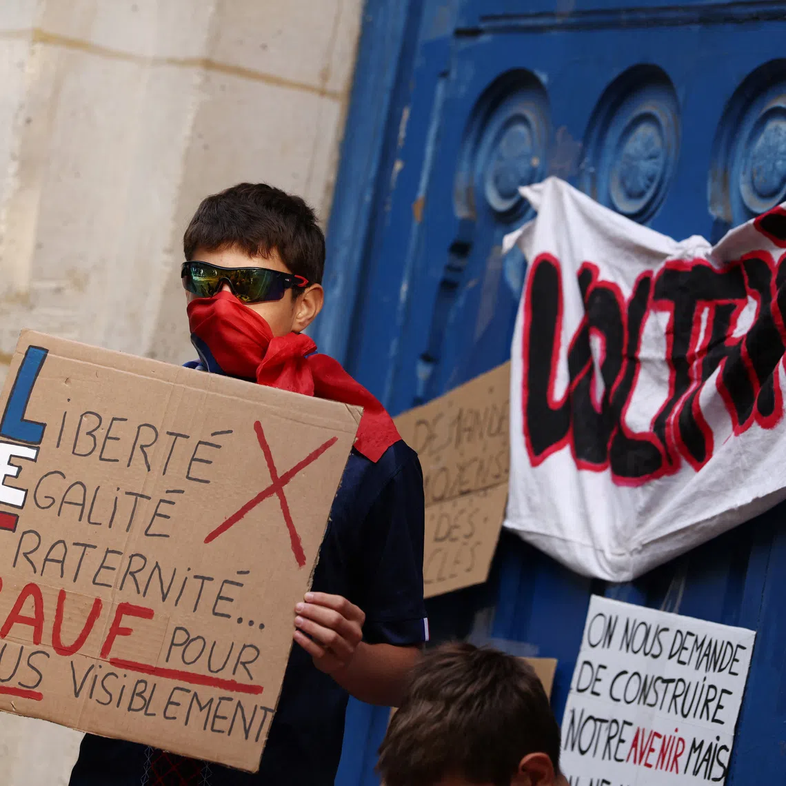 A masked high school student holds a placard reading \"Liberty, Equality, Fraternity. Except for us, apparently\" during a gathering outside the Lycee Voltaire high school in Paris as part of a nationwide day of demonstrations and blockades, voicing anger over overcrowded classrooms, teacher shortages and dilapidated school buildings, which students blame on years of underinvestment, France, October 6, 2026. REUTERS/Tom Nicholson