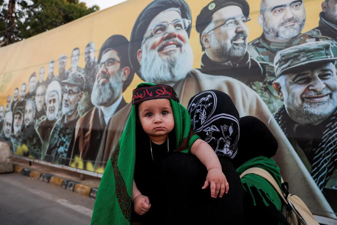 Women carrying a child walk past a mural depicting former Hezbollah leader Hassan Nasrallah and other senior figures, on the outskirts of Beirut, Lebanon, on June 17, 2026. 