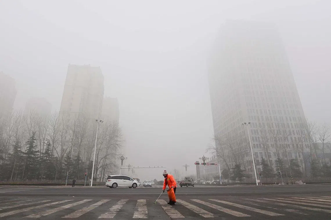 A street cleaner working as fog and air pollution shroud buildings in Qingzhou, in China's eatern Shandong province on Dec 28, 2023. 