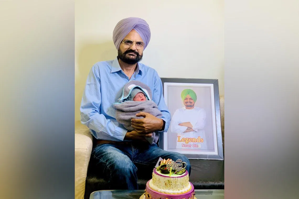 Mr Balkaur Singh holding his newborn son while sitting next to a photo of his late son Shubhdeep, or Sidhu Moose Wala, a popular singer who was killed in 2022.