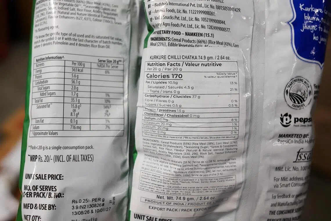 A Maharashtra Food and Drug Administration official displays two packets of Kurkure chips, one with the original nutrition information (left) and another with a modified nutrition information sticker (right).