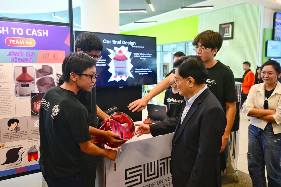 Student Jonathan Liang (in black, right) and teammates showing DPM Heng Swee Keat the design of their burner filter system with ash collection box on Sept 9.