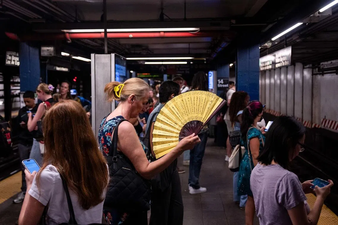 A commuter uses a hand fan at the 14th Street-Union Square subway station during high temperatures in New York city on June 23, 2025. 