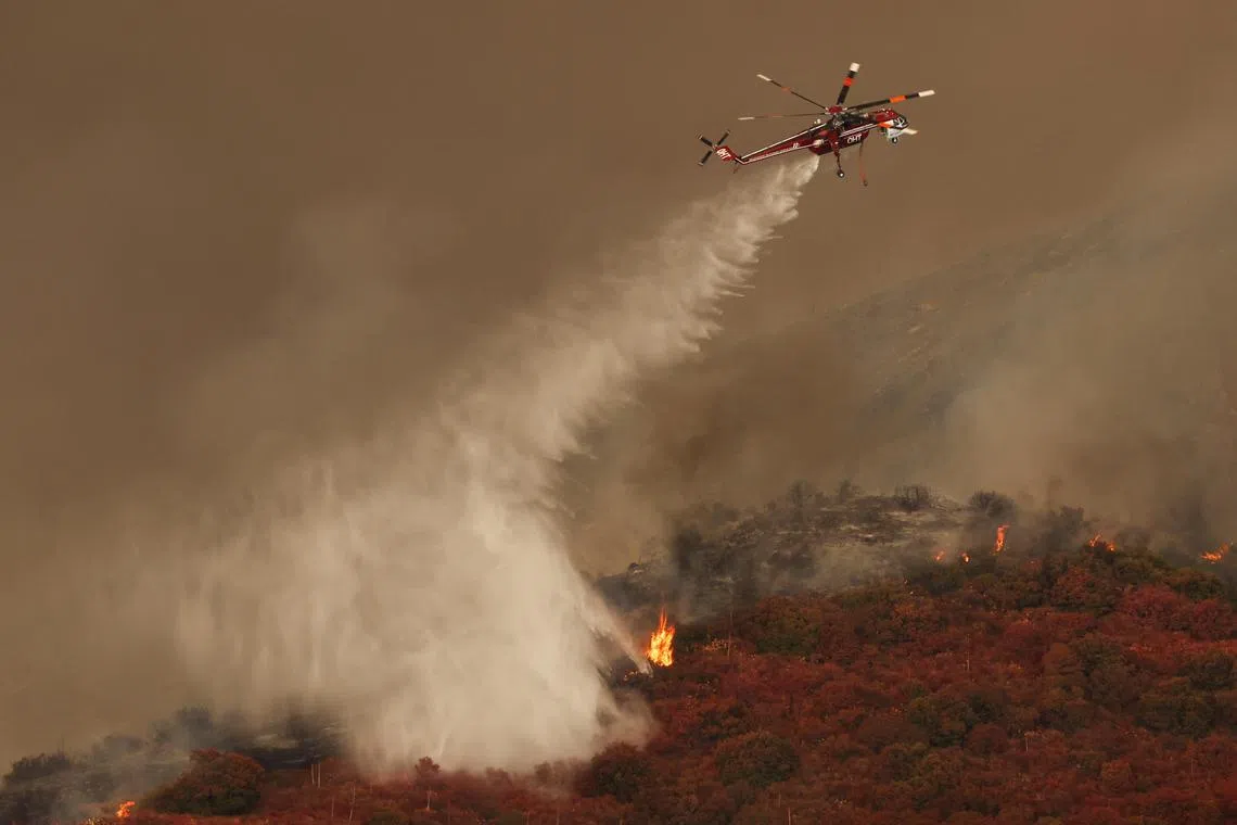A helicopter combats the Airport Fire, a wildfire burning in the hills of Orange County, California.