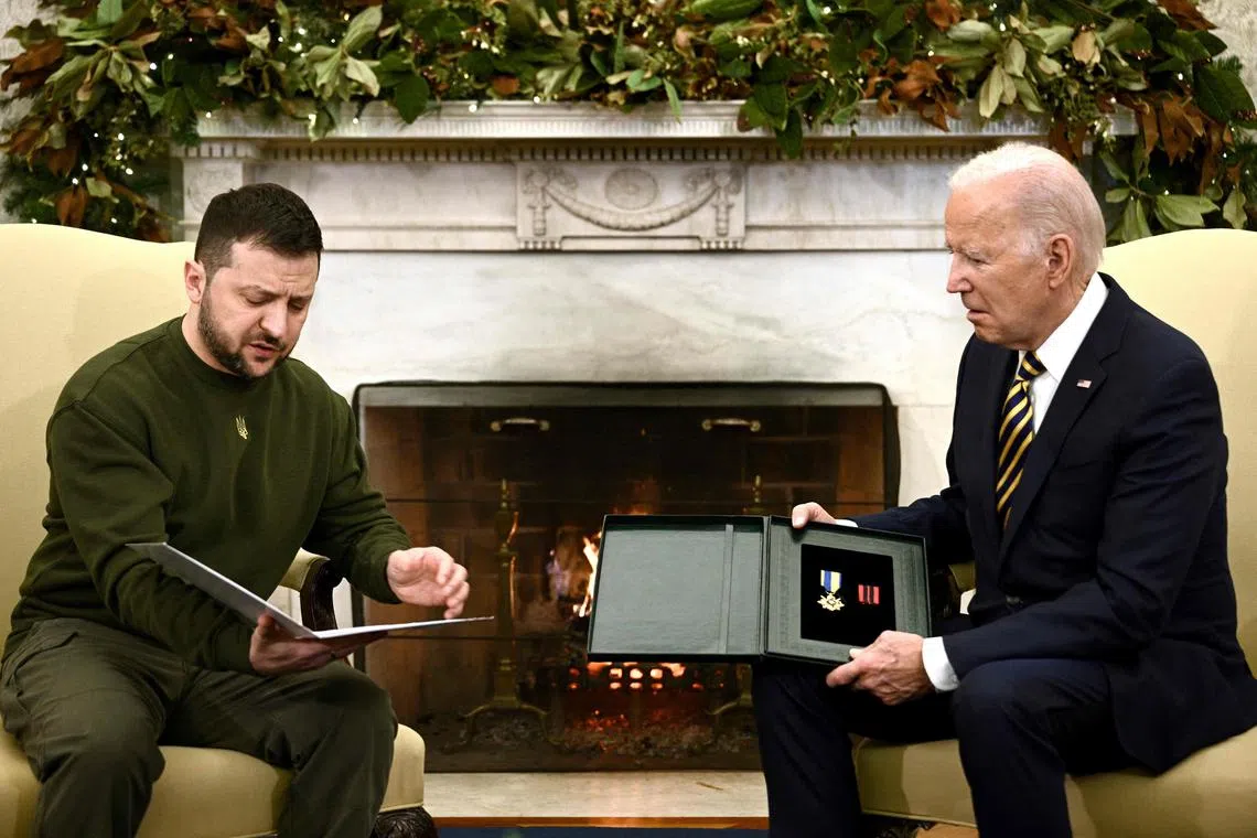 TOPSHOT - Ukraine's President Volodymyr Zelensky presents a Ukrainian military medal (The Cross for Military Merit) to US President Joe Biden in the Oval Office of the White House, in Washington, DC on December 21, 2022. - Zelenskyy mentioned this particular medal was awarded earlier this year to a Ukrainian officer for outstanding feats on the battlefield. The officer met earlier this week with President Zelenskyy in Bakhmut and asked him to give his medal to President Biden as a token of his profound gratitude. The officer also wrote President Biden a letter expressing Ukraine's appreciation for America's assistance that helped keep many people in Ukraine alive. Zelensky is in Washington to meet with US President Joe Biden and address Congress -- his first trip abroad since Russia invaded in February. (Photo by Brendan SMIALOWSKI / AFP)