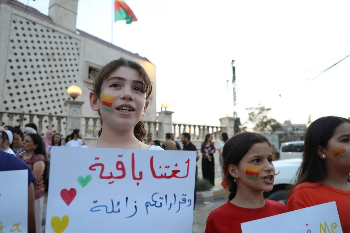 A girl holds a sign reading \"Our language remains, your decisions will fade\" during a gathering in Qamishli, Syria, August 31, 2026. REUTERS/Orhan Qereman