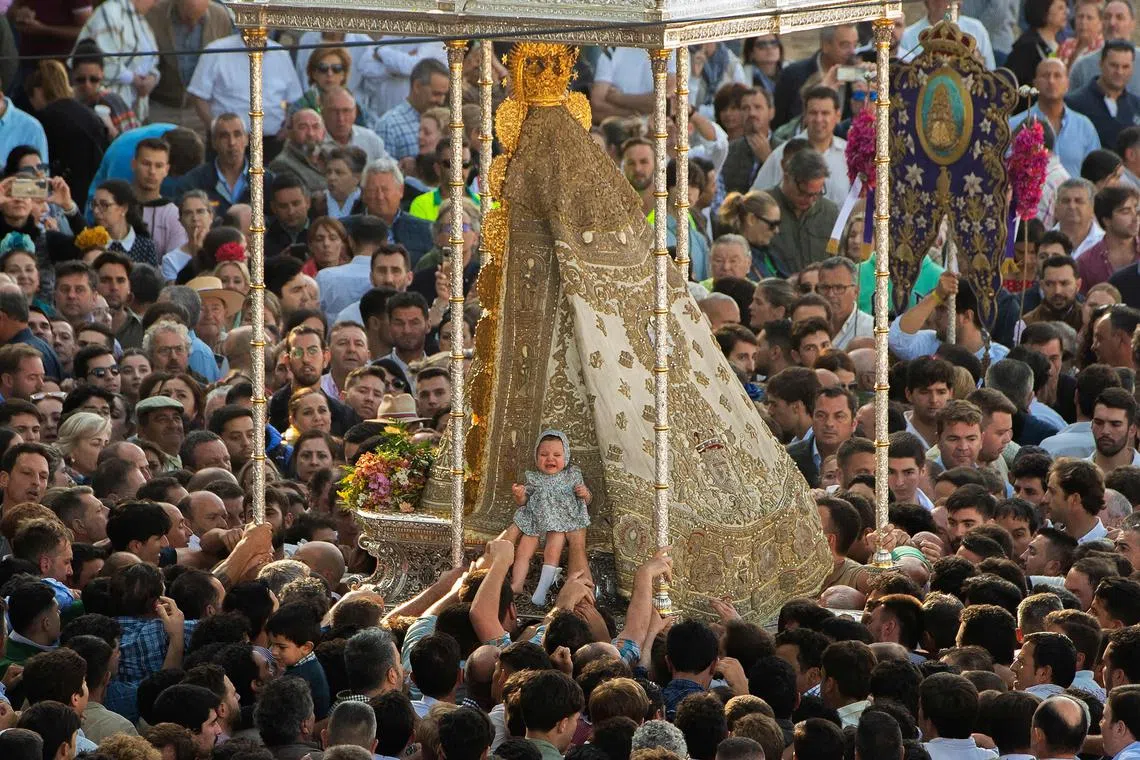 Pilgrims placing a baby against the effigy of the Rocio Virgin outside the hermitage in El Rocio village in the Andalusian province of Huelva on May 29, 2023. The annual El Rocio pilgrimage, the largest in Spain, gathers hundreds of thousands of devotees in traditional outfits converging in a burst of colour as they make their way on horseback and on board decorated carriages across the Andalusian countryside. 