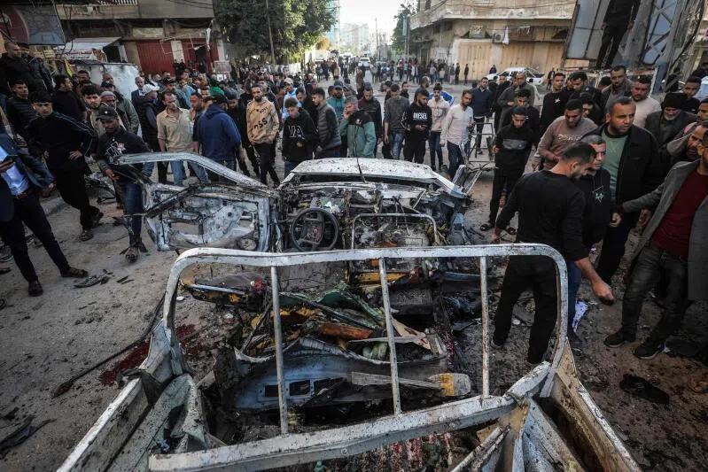 People gather around a destroyed Palestinian police jeep that was targeted by an Israeli air strike in Nuseirat refugee camp in the central Gaza Strip on March 22, 2026.