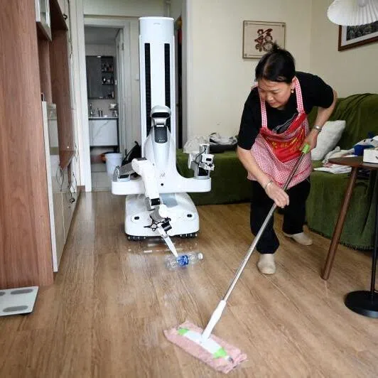 An X Square robot carrying a bottle to a rubbish bin as a housekeeper cleans the floor at a customer’s home in Beijing.