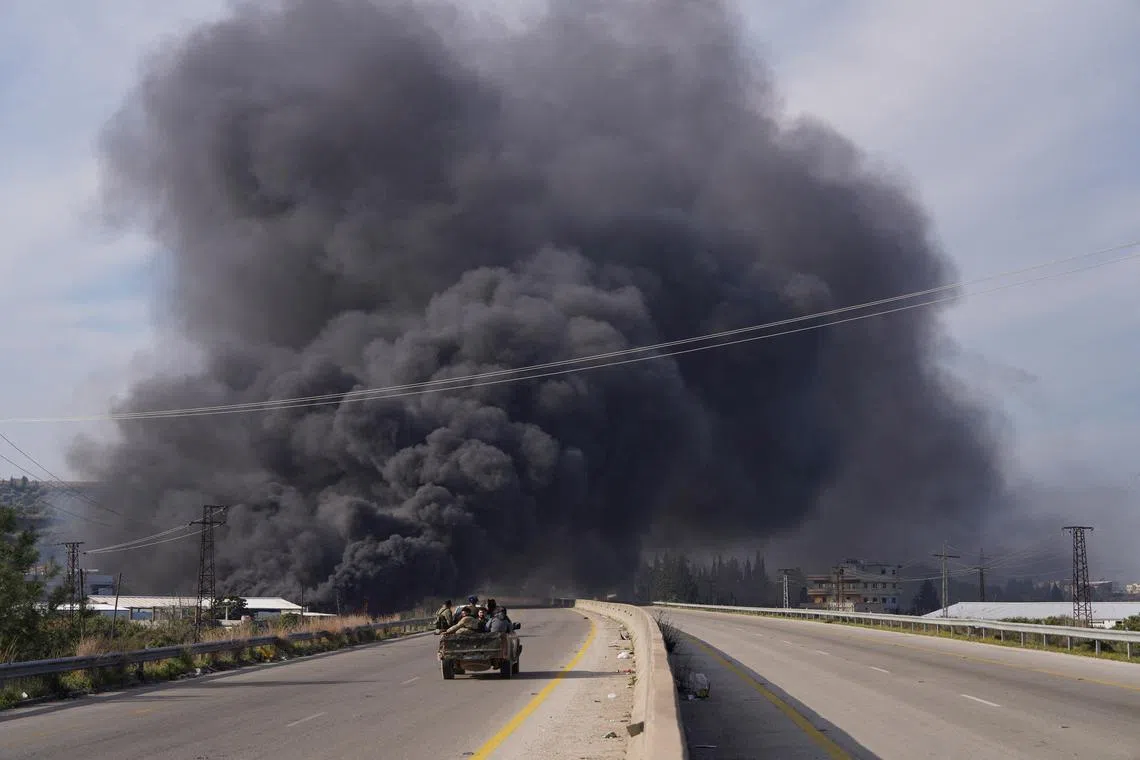 Smoke rises while members of the Syrian forces ride on a vehicle as they battle against a nascent insurgency by fighters from ousted leader Bashar al-Assad's Alawite sect, in Latakia, Syria March 7, 2025. REUTERS/Karam al-Masri