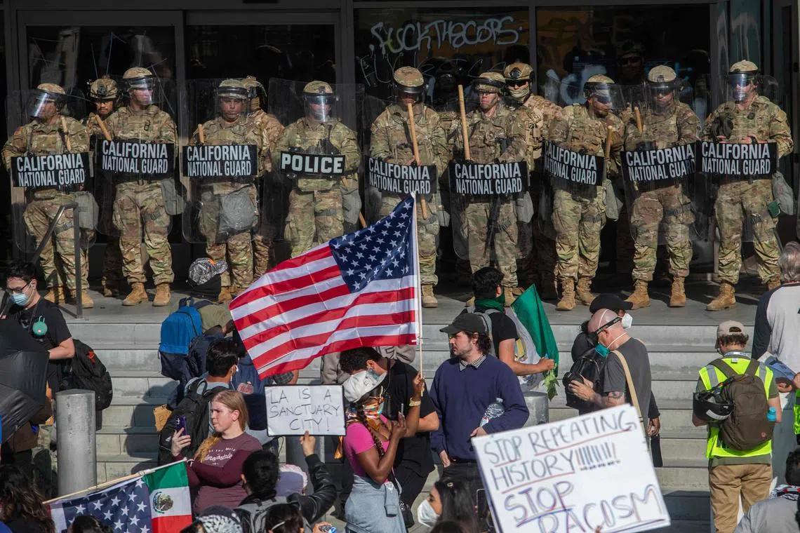 (FILES) Demonstrators holding signs and flags face California National Guard members standing guard outside the Federal Building as they protest in response to federal immigration operations in Los Angeles, on June 9, 2025. US Defense Secretary Pete Hegseth has ordered the withdrawal of 2,000 National Guard troops from Los Angeles, roughly halving the contentious deployment in the city, the Pentagon said on July 15, 2025. President Donald Trump ordered thousands of National Guard and hundreds of Marines into Los Angeles last month in response to protests over federal immigration sweeps -- a move opposed by city leaders and California's Democratic Governor Gavin Newsom. (Photo by Apu GOMES / AFP)