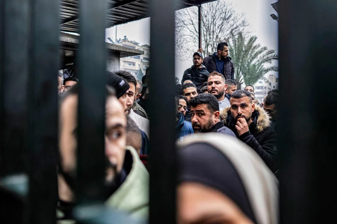 Men queue up as former soldiers, police members, and civilians wait at a centre for handing over small arms and security registration with the new authorities in Damascus on Dec 24.  