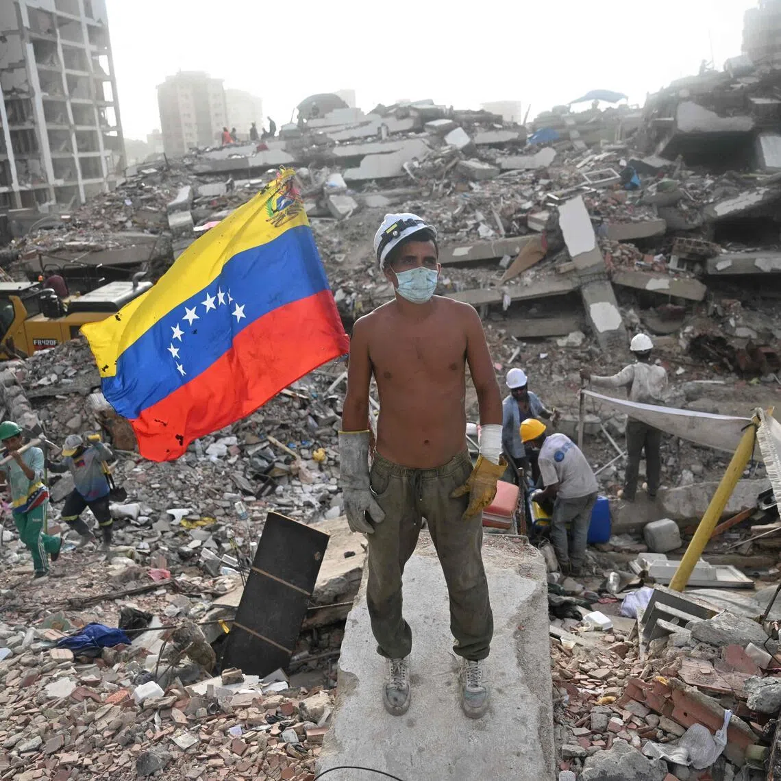 A volunteer rescuer stands next to a Venezuelan flag on debris from a collapsed building in La Guaira state, Venezuela.