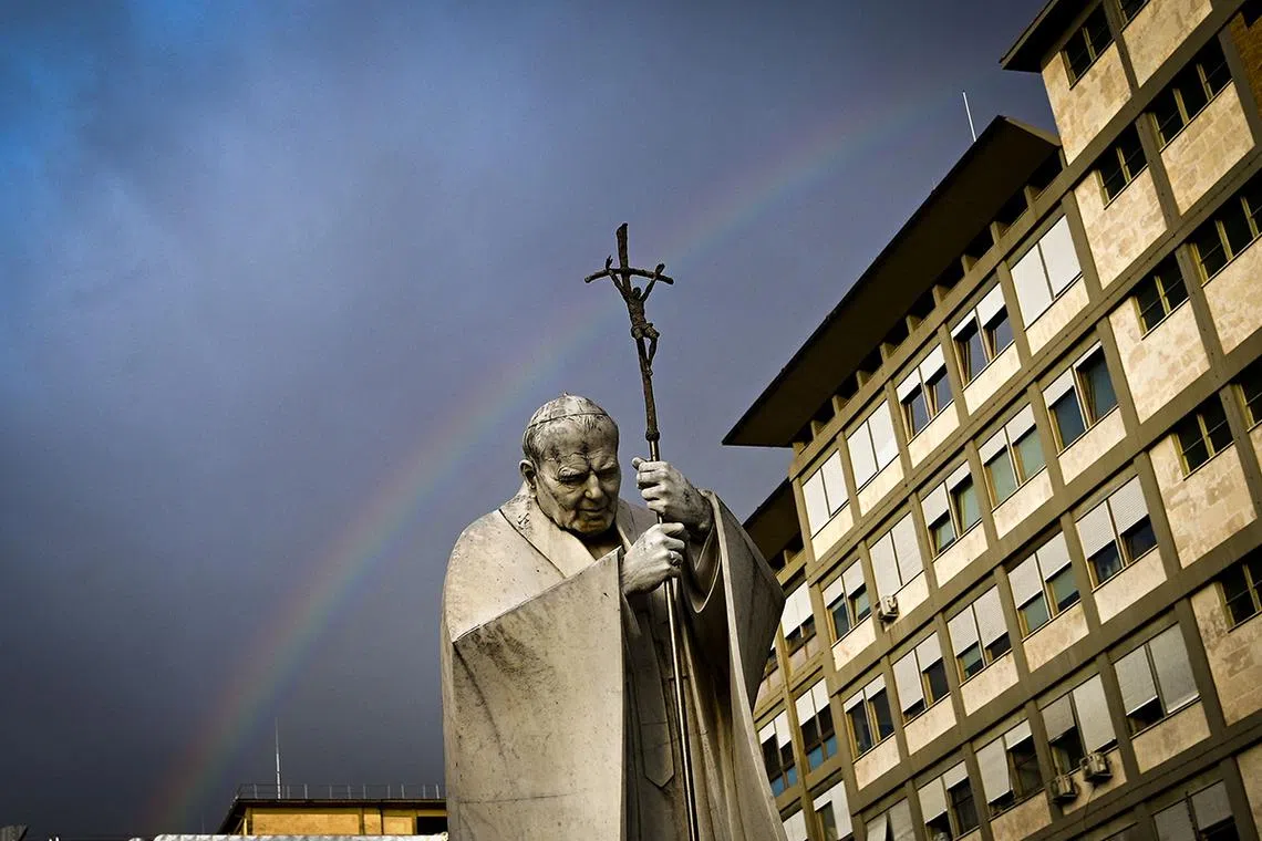 TOPSHOT - A rainbow appears above a statue of Pope John Paul II outside the Gemelli hospital where Pope Francis is hospitalised for tests and treatment for bronchitis in Rome, on February 18, 2025. The Vatican on February 18, 2025 cancelled two of Pope Francis's events at the weekend as the 88-year-old continues to receive hospital treatment for bronchitis. (Photo by Tiziana FABI / AFP)