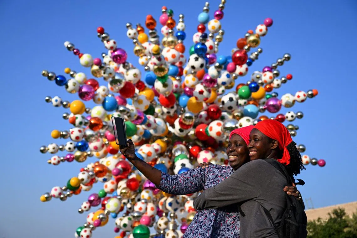 A handout picture released by the Qatar Foundation shows women taking a selfie in front of an artwork entitled "Come Together", by South Korean artist Choi Jeong-hwa, at Education City Stadium in al-Rayyan, west of Doha, on December 13, 2022. The 12-metre tall sculpture is made out of workers' helmets, footballs and traditional Qatari objects, and pays tribute to all those in Qatar who helped to realise the FIFA World Cup Qatar 2022. It is part of Qatar Foundation's collection of public art that includes over 150 artworks by local and international artists, including the final artwork of M.F. Husain. 