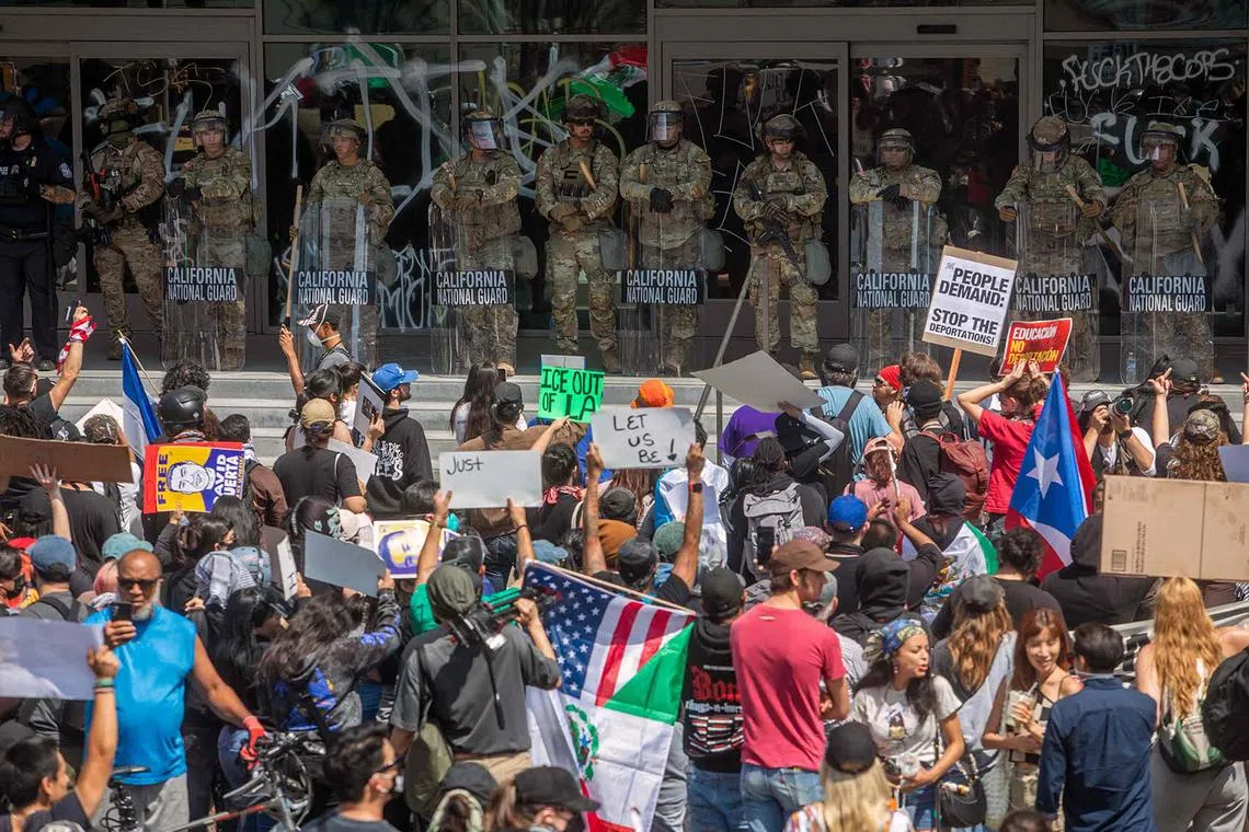 Demonstrators holding signs and flags, facing National Guard standing guard outside the Federal Building, as they protest in response to federal immigration operations in Los Angeles, on June 9, 2025. US President Donald Trump on June 9 ordered active-duty Marines into Los Angeles, vowing those protesting immigration arrests would be "hit harder" than ever. 