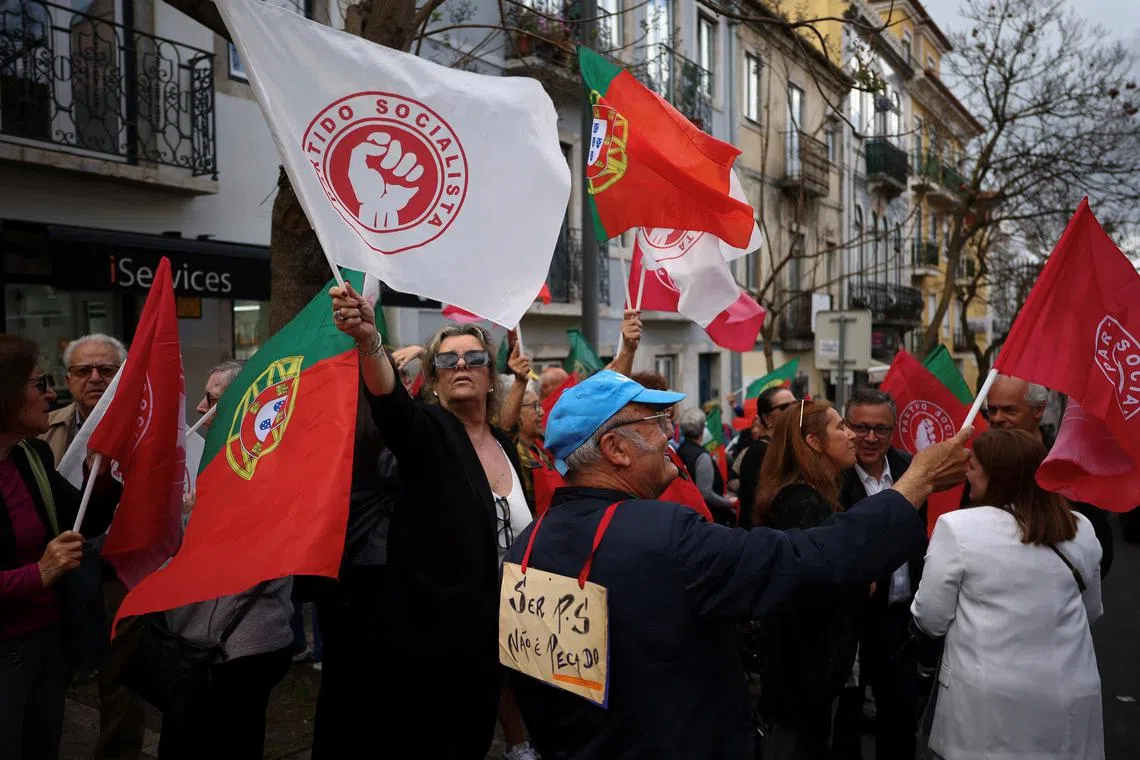People wave flags of the Socialist party (PS) as a man wears a card reading, \"To be socialist is not a sin\", while waiting for PS leader Pedro Nunes Santos, for a rally ahead of the snap elections, in Lisbon, Portugal, May 13, 2025. REUTERS/Pedro Nunes