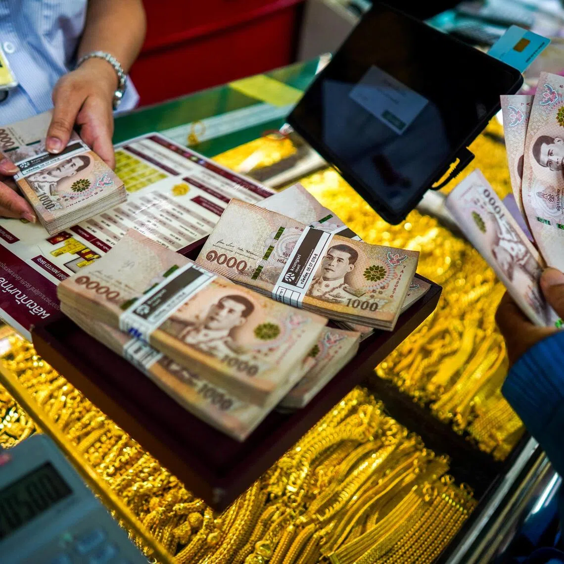 A customer and an employee count Thai baht banknotes at a gold shop in Bangkok's Chinatown, Thailand, October 9, 2025. REUTERS/Athit Perawongmetha