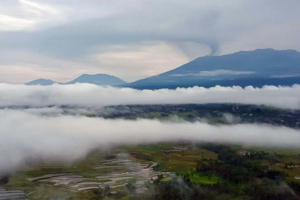 TOPSHOT - An aerial view shows Mount Marapi (background R) spewing volcanic ash during an eruption as seen from Batusangkar in Agam, West Sumatra, at dawn on December 6, 2023. The death toll from a volcano eruption in Indonesia has risen to 22 after nine more bodies were discovered, a search and rescue agency official said December 5. (Photo by ADI PRIMA / AFP)