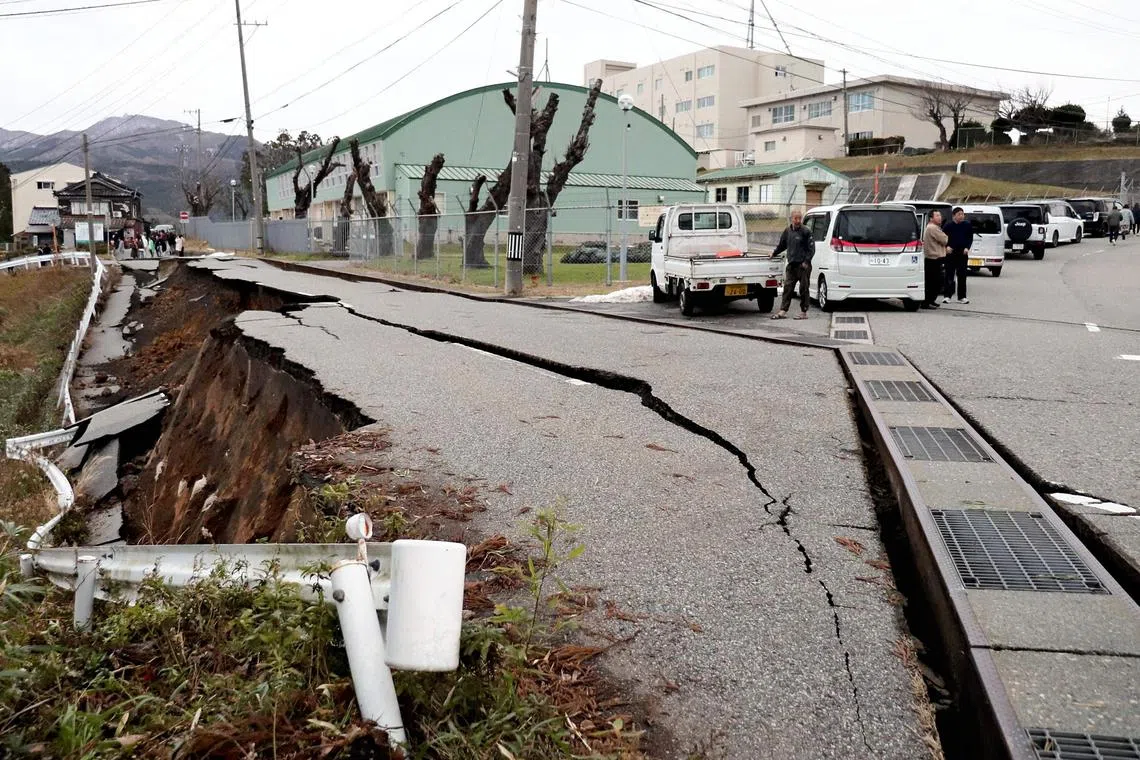 People standing next to large cracks in the pavement after evacuating into a street in the city of Wajima, Ishikawa prefecture on Jan 1, 2024, following an earthquake.