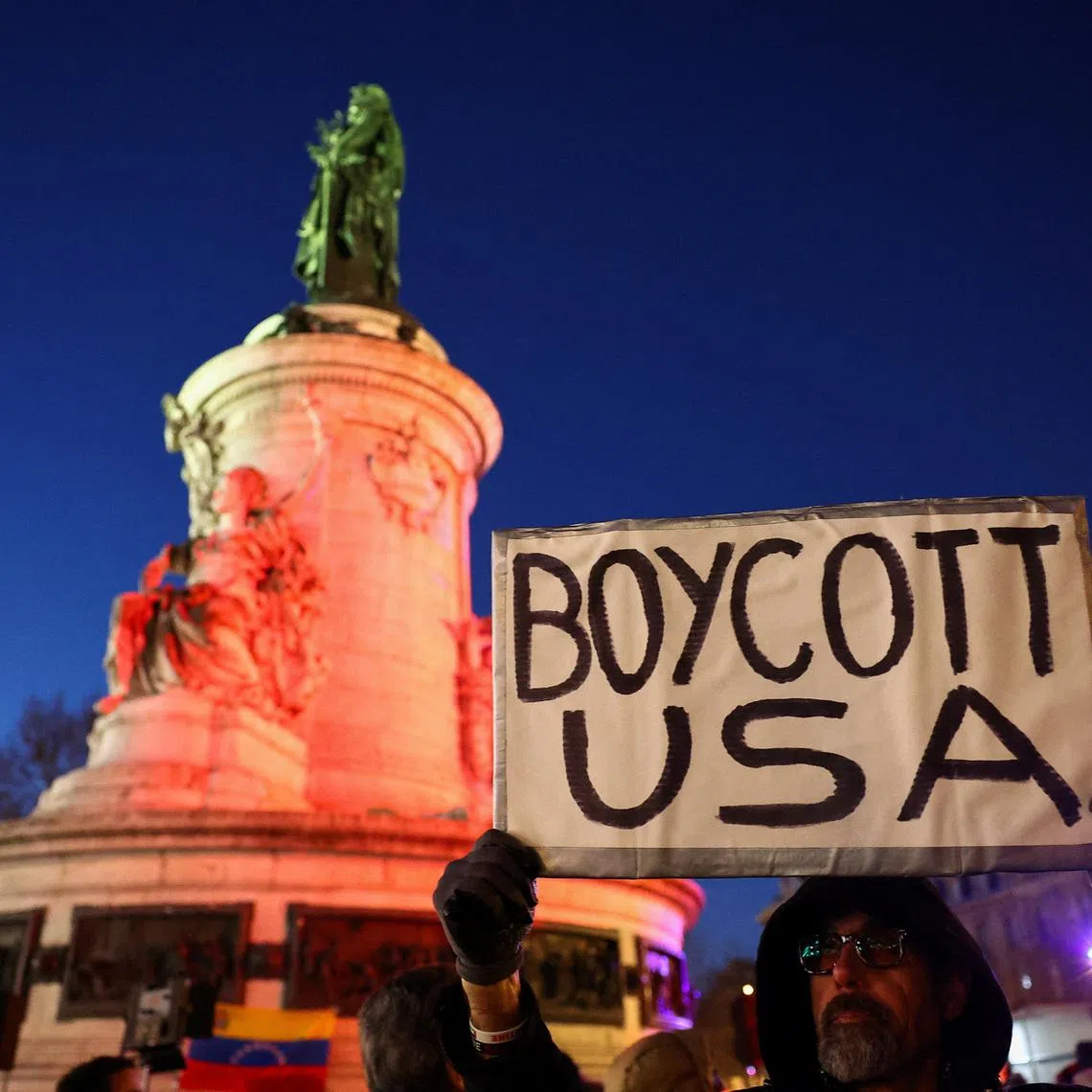 A man holds up 'Boycott USA' sign, as people demonstrate to oppose U.S. actions in Venezuela at a protest, after U.S. President Donald Trump said the U.S. has struck Venezuela and captured its President Nicolas Maduro, in Paris, France, January 3, 2026. REUTERS/Abdul Saboor