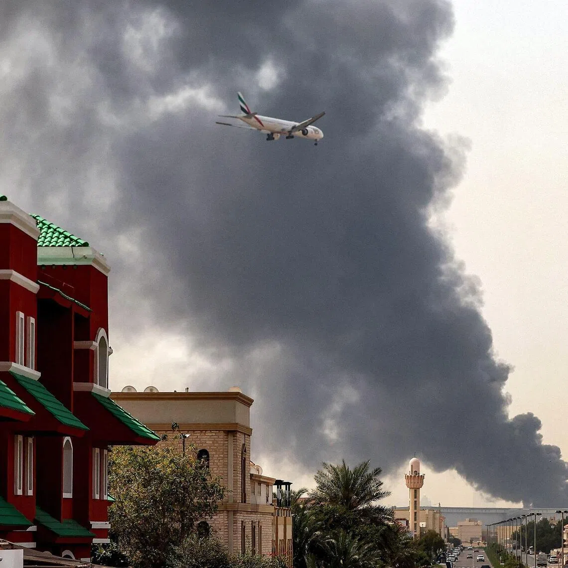 TOPSHOT - An Emirates aircraft prepares for landing as a smoke plume rises from an ongoing fire near Dubai International Airport in Dubai on March 16, 2026. Flights were gradually resuming at Dubai airport on March 16, previously the world's busiest for international flights, the airport operator said, after a "drone-related incident" sparked a fuel tank fire nearby, as Iran kept up its Gulf attacks. (Photo by AFP) / 