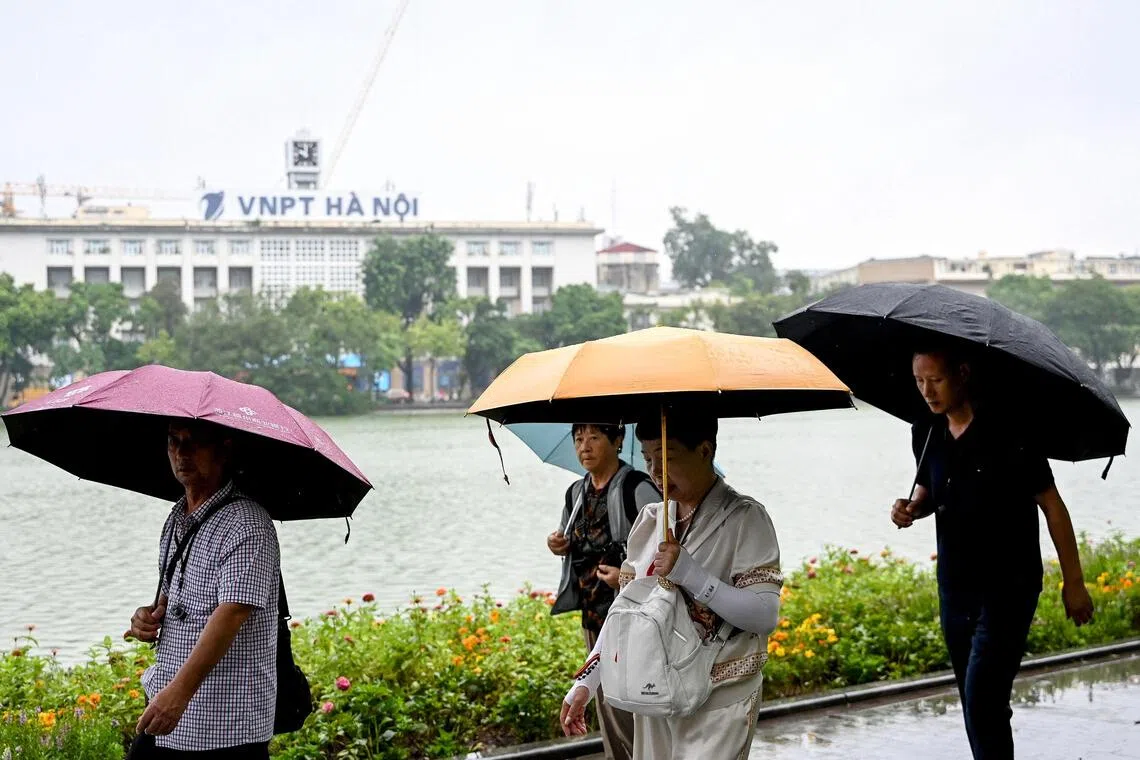Tourists walk under umbrellas to shelter from the rain along Hoan Kiem Lake in Hanoi on October 14, 2025. (Photo by Nhac NGUYEN / AFP)