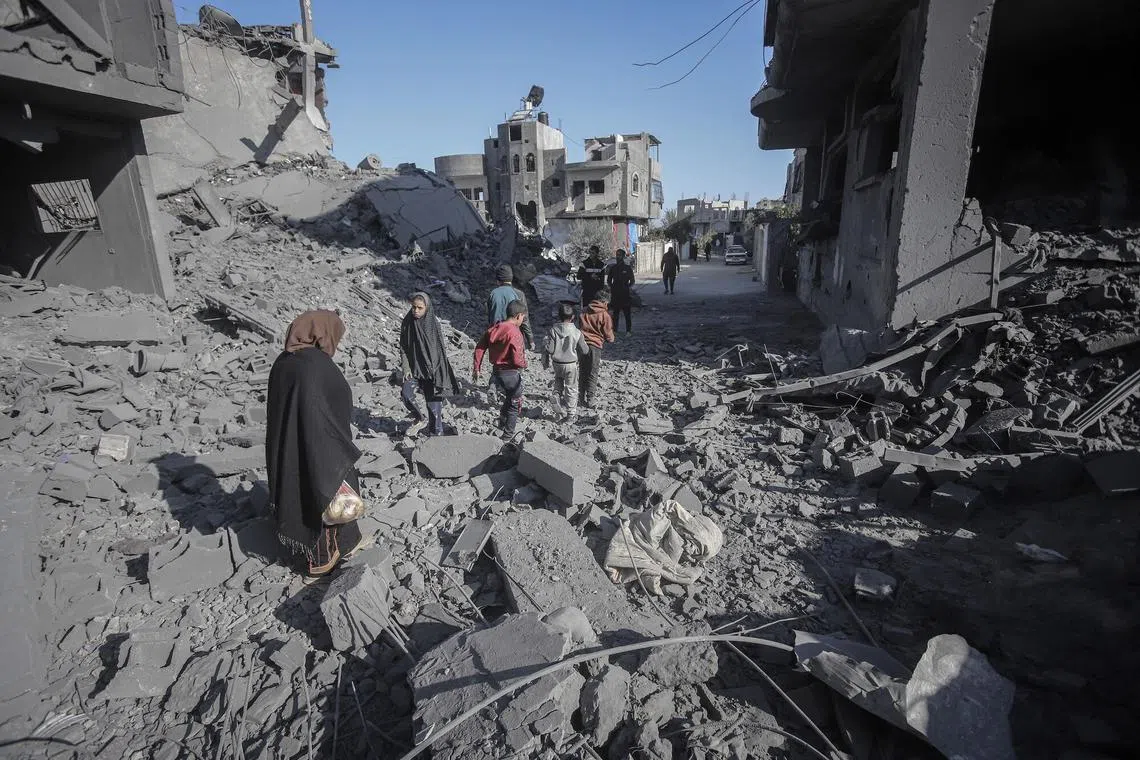 Palestinians walk across building debris following an Israeli airstrike at the Nuseirat refugee camp in central Gaza, on Jan 3.