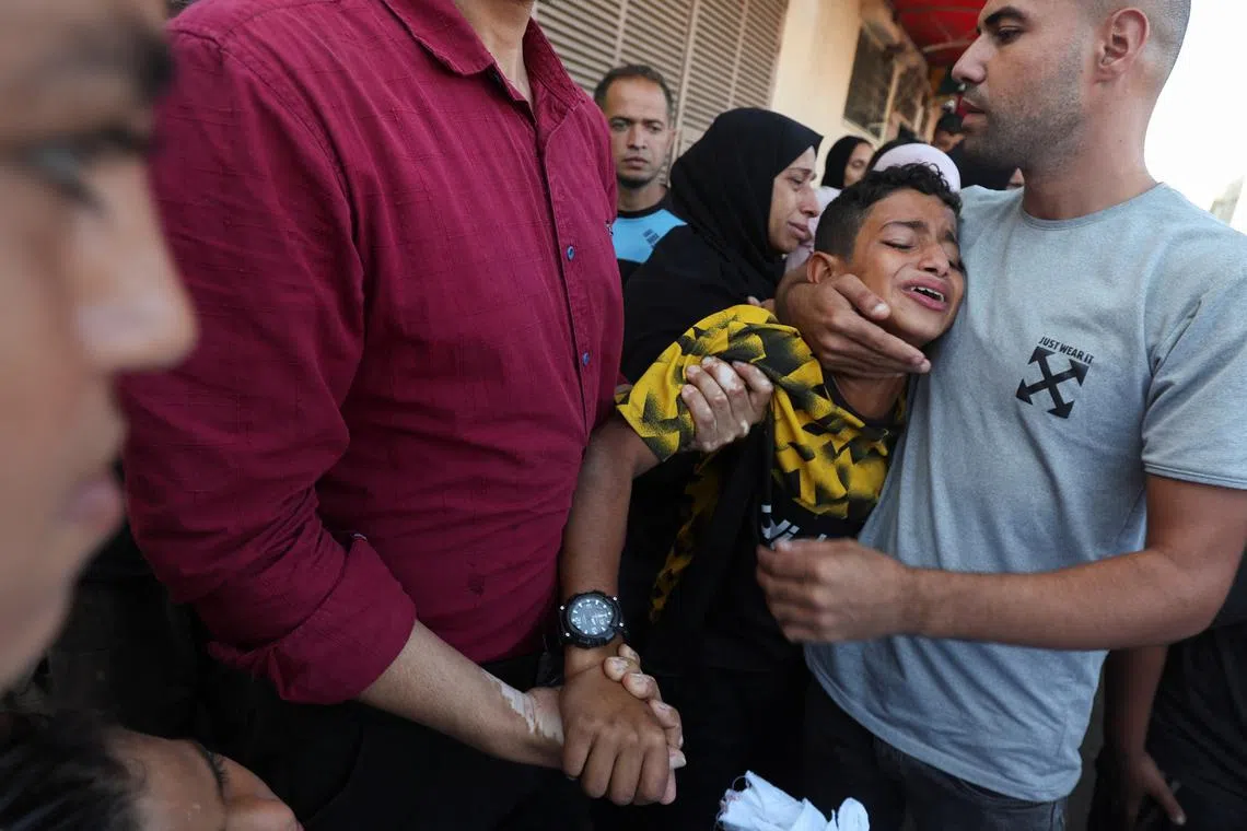 A boy is comforted as he mourns near the body of his father and other Palestinians, who were killed in an Israeli strike, amid the Israel-Hamas conflict, at Al-Aqsa Martyrs Hospital in Deir Al-Balah in the central Gaza Strip, October 9, 2024. REUTERS/Ramadan Abed