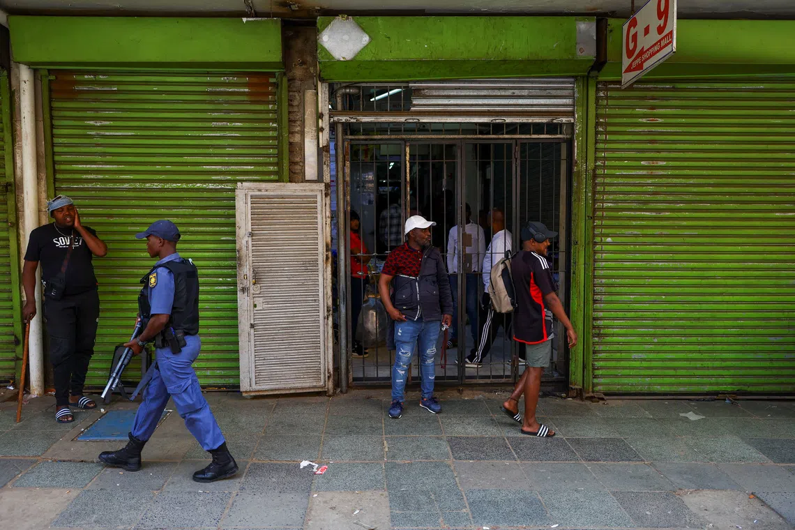 A police officer carrying a weapon walks past a shop as police maintain a presence during a march following anti-migrant unrest in Johannesburg and the coastal city of Durban, where vehicles were torched and foreign-owned shops were looted, in Johannesburg, South Africa, October 9, 2026. REUTERS/Siphiwe Sibeko