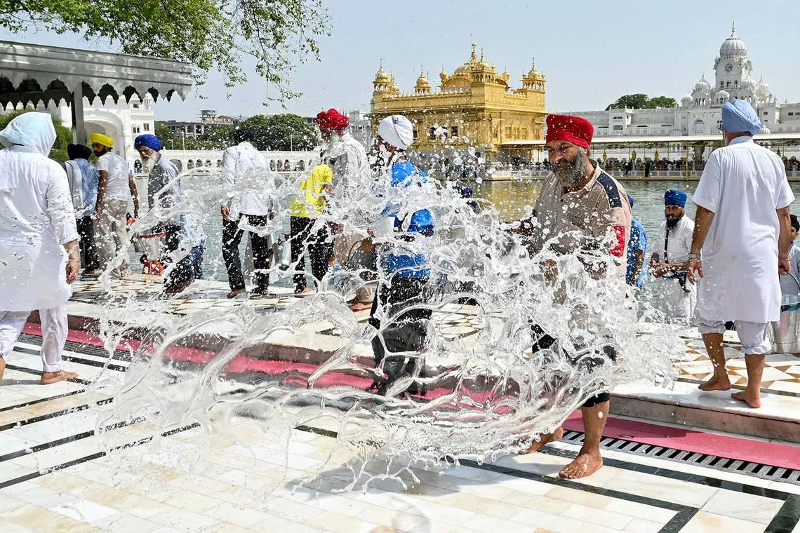 Sikh volunteers splashing buckets of water to cool off the floor at the Golden Temple on a hot summer day in Amritsar, India, on June 11, 2025. 